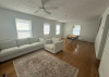 Living Room with beige couch and large windows in the far corner there is a small dining table